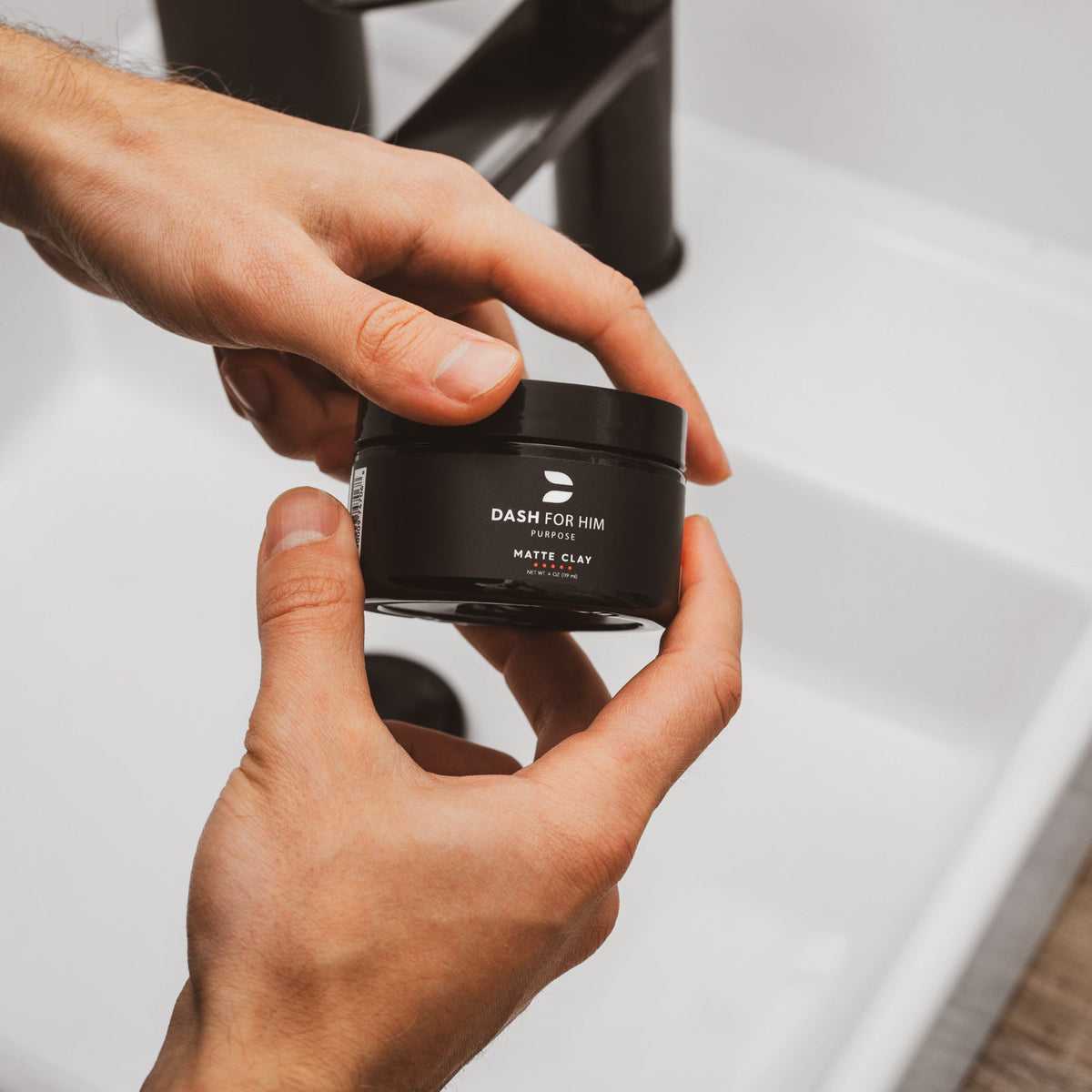 Holding a jar of DASH FOR HIM Matte Clay at the bathroom sink